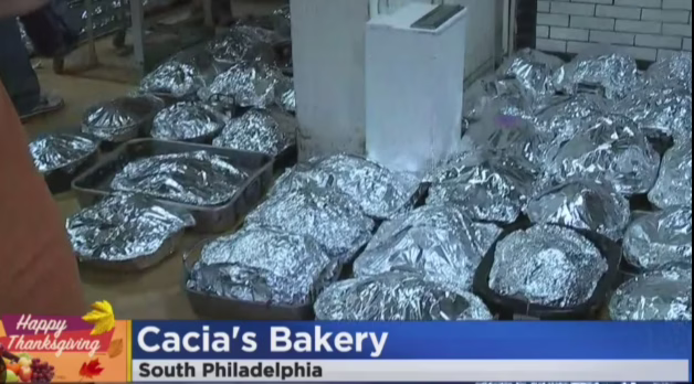Dozens of foil-wrapped Thanksgiving turkeys lined up in roasting pans on the floor at Cacia’s Bakery in South Philadelphia, shown during a holiday news segment.